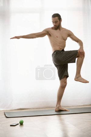 Foto de Hombre guapo practicando yoga en una esterilla en su casa durante la mañana. - Imagen libre de derechos