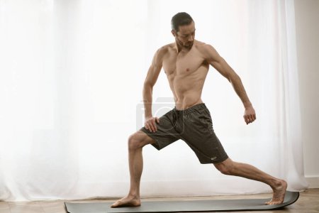 Téléchargez les photos : Beau homme debout sur le tapis de yoga devant la fenêtre. - en image libre de droit