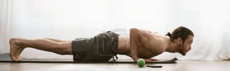 Foto de Un hombre guapo hace ejercicios en una esterilla de yoga, haciendo flexiones en casa por la mañana.. - Imagen libre de derechos