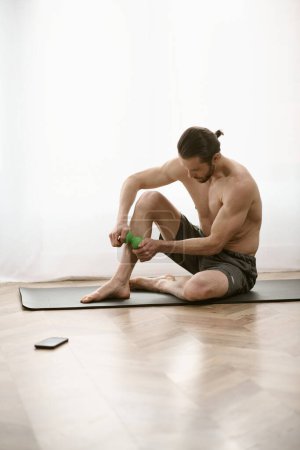 Schöner Mann sitzt auf Yogamatte und hält Massageball in beruhigender Pose.