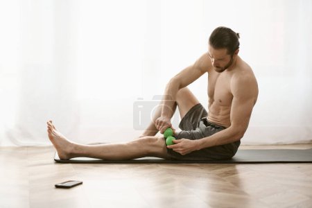 Un hombre se sienta en el suelo, sosteniendo una bola de masaje en su mano, practicando yoga en casa.