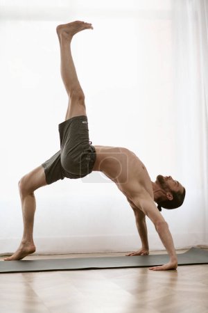 A handsome man practices a handstand on a yoga mat in his home.