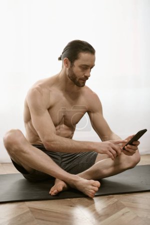 Hombre guapo, en casa, hace yoga pacíficamente mientras usa el teléfono celular.