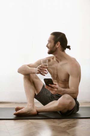 A man sits on a yoga mat, peacefully holding a cell phone.