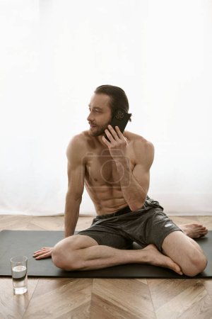 Hombre guapo en estera de yoga charlando en el teléfono celular durante la rutina de la mañana.