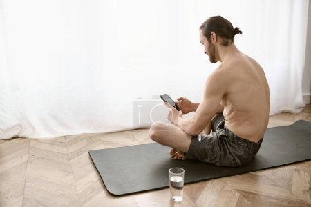 A man sitting on a yoga mat, using a cell phone.