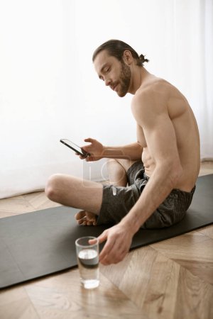 Téléchargez les photos : Homme torse nu sur tapis de yoga, absorbé dans le téléphone. - en image libre de droit