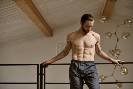 Shirtless man perched on staircase rail at home.