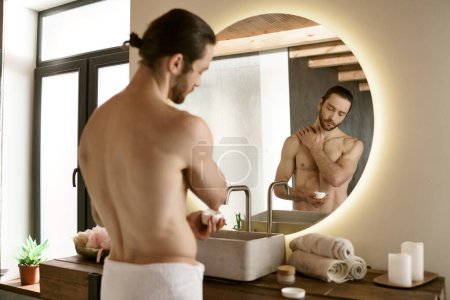 Téléchargez les photos : Un homme se tient devant un miroir de salle de bain, appliquant des produits de soins de la peau. - en image libre de droit