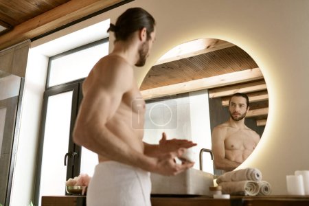 Hombre guapo en el baño, dedicándose a la rutina de cuidado de la piel de la mañana y aseo delante del espejo.