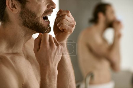 A man with a handsome face brushes his teeth in front of a mirror.
