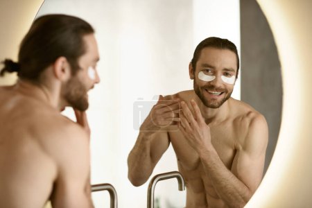 Téléchargez les photos : Beau homme appliquant des patchs, une partie de la routine de soins de la peau du matin à la maison. - en image libre de droit