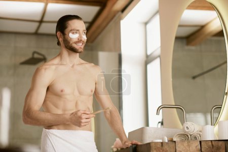 Foto de Un hombre en toalla, haciendo rutina matutina de cuidado de la piel, parado frente al espejo. - Imagen libre de derechos