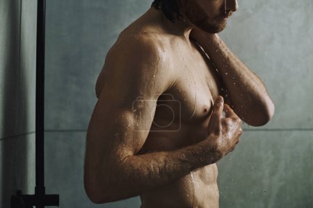 Shirtless man stands before shower, part of his morning skincare routine.