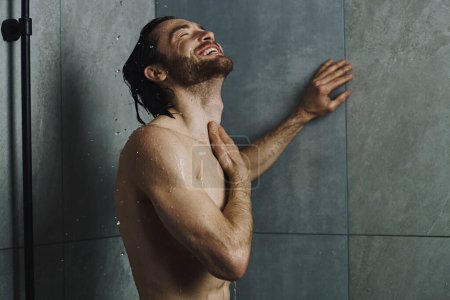Ein Mann steht unter der Dusche, die Hände erhoben, umarmt das Wasser.