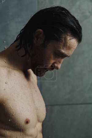 Foto de Un hombre sin camisa se para ante una ducha, preparándose para su rutina matutina.. - Imagen libre de derechos