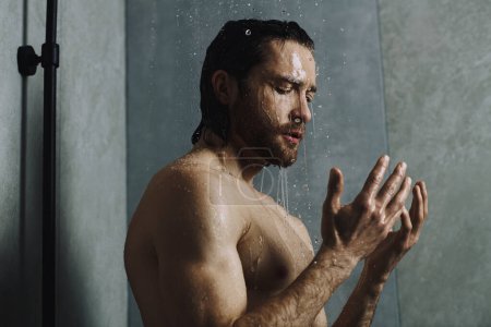 Foto de A man standing in a shower with his hands in the air, enjoying his morning routine. - Imagen libre de derechos