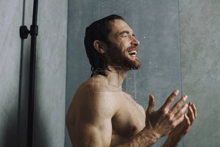 Handsome man standing in the shower with arms raised, part of his morning routine.