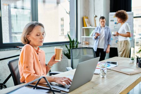 Téléchargez les photos : Femme profiter du café tout en travaillant sur ordinateur portable, avec ses collègues divers sur toile de fond. - en image libre de droit