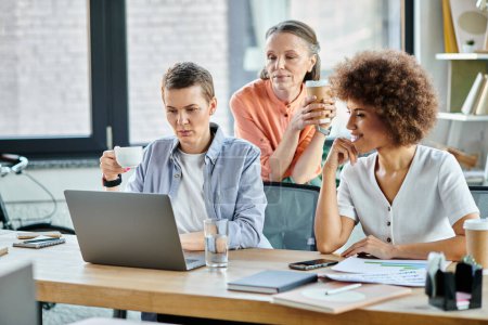 Groupe diversifié de femmes d'affaires travailleuses à une table avec un ordinateur portable dans un espace de coworking.
