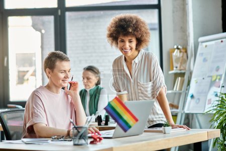 Téléchargez les photos : Attractive diverse businesswomen working together on project in office, pride flag. - en image libre de droit