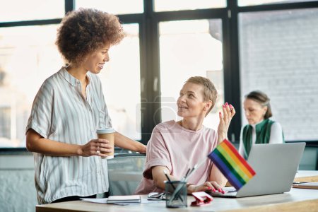 Cheerful diverse businesswomen working together on project in office, pride flag.