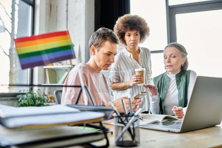Mujeres de negocios atentas y diversas, incluyendo miembros de la comunidad LGBT, trabajando intensamente alrededor de una computadora portátil en una oficina.