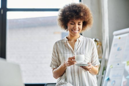 Téléchargez les photos : Femme afro-américaine, élégante et concentrée, se détend avec une tasse de café fumante à la main. - en image libre de droit