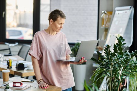 Femme attrayante, dans une chemise rose vif, travaille avec diligence sur un ordinateur portable.