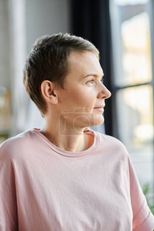 A woman gazes out a window wearing a pink shirt.