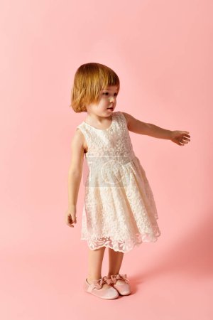 Little girl in white dress posing on pink background.
