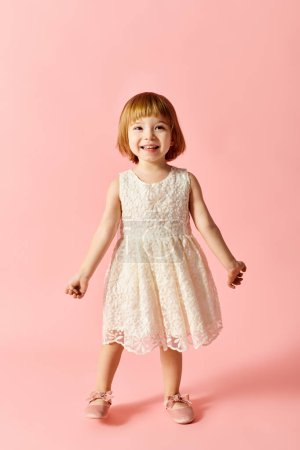Little girl in white dress poses gracefully on pink backdrop.