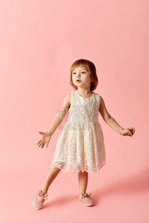 Kleines Mädchen in weißem Kleid posiert auf leuchtend rosa Hintergrund.