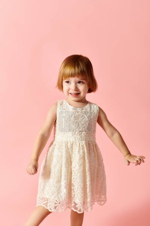 Adorable fille en robe blanche posant en toute confiance sur fond rose.