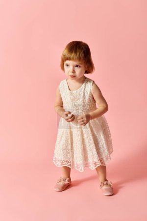 Kleines Mädchen im weißen Kleid posiert auf rosa Hintergrund.