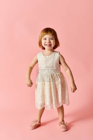 Photo for Adorable child wearing white dress, standing on pink background. - Royalty Free Image