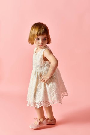 Photo for Little girl in white dress standing on pink backdrop. - Royalty Free Image