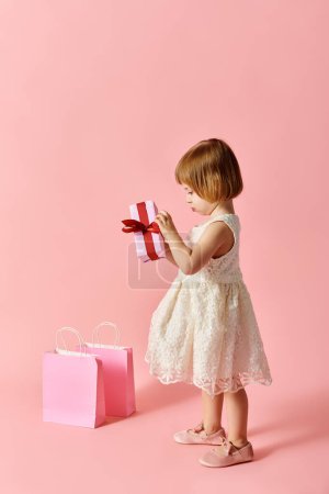 Kleines Mädchen im weißen Kleid hält freudig eine rosa Geschenkschachtel in der Hand.