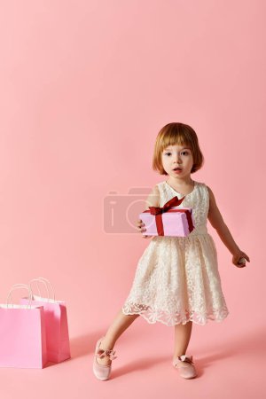 Téléchargez les photos : Petite fille en robe blanche tenant boîte cadeau rose. - en image libre de droit