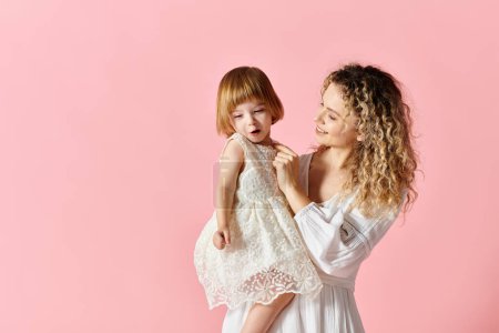 Photo for Mother in white dress holding girl in white dress on pink background. - Royalty Free Image