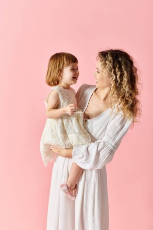 Una mujer sosteniendo a su hija sobre un suave fondo rosa.