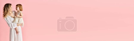 Photo for A woman in a pink background cradling her baby girl in her arms. - Royalty Free Image