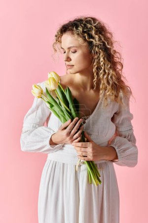 Stylish woman with curly hair holding colorful tulip bouquet on pink background.