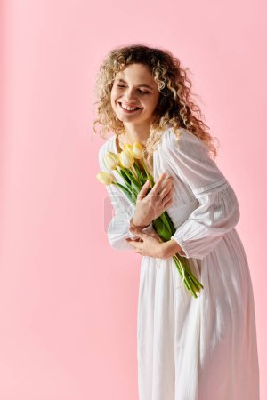 Femme en robe blanche tenant bouquet de tulipes.
