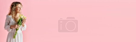Téléchargez les photos : Une femme tient un bouquet de fleurs sur un fond rose. - en image libre de droit