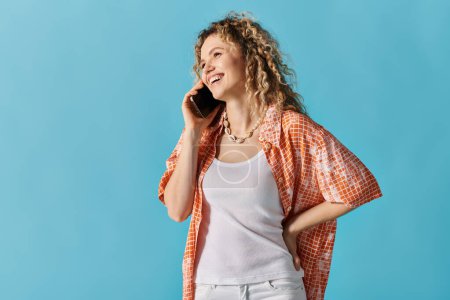 Woman with curly hair talking on cell phone against vibrant blue background.