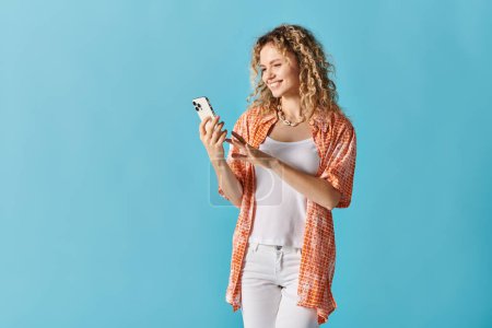 Young woman with curly hair using a cell phone on blue background.
