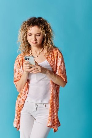 Eine modische Frau mit lockigem Haar ist in ihr Handy vertieft.