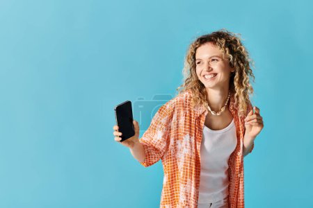 Young woman with curly hair smiling while holding smartphone.