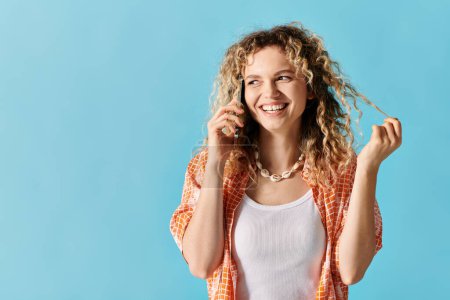 Young woman with curly hair talking on phone against blue background.